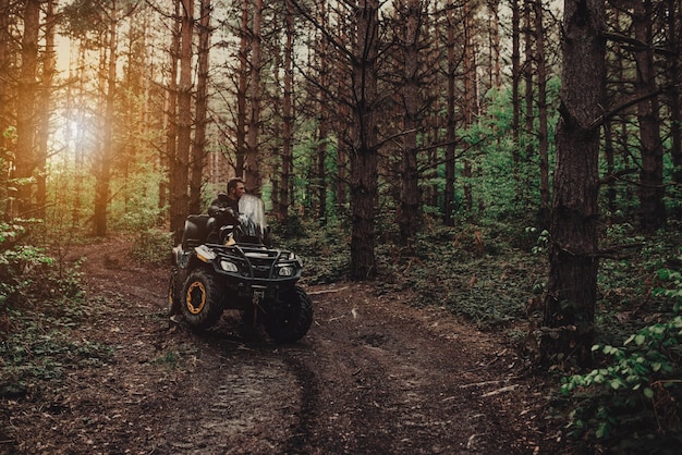 Ein junger Mann in einem weißen Helm fährt auf einem Quad-Bike durch den Wald. Extremes Hobby. Ein Ausflug zum ATV auf der Straße von Baumstämmen