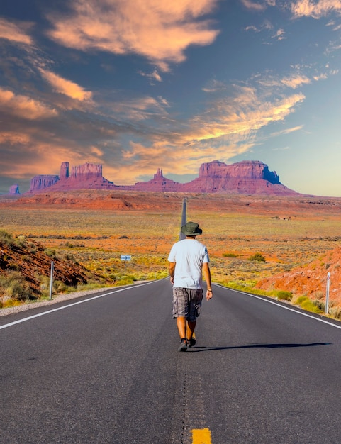 Ein junger Mann in einem weißen Hemd, der im Sonnenuntergang auf der Straße zum Monument Valley geht. Utah