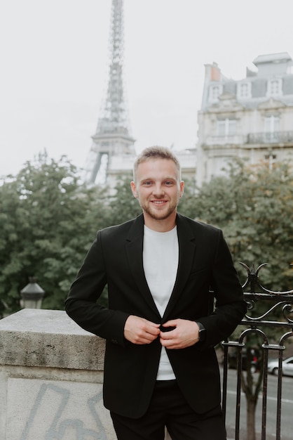 Ein junger Mann in einer dunkelschwarzen Jacke steht im Hintergrund des Eiffelturms