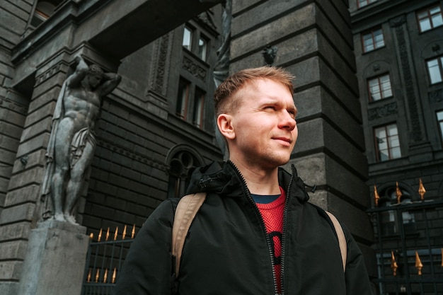 Ein junger Mann in einer Jacke an der Wand eines dunklen historischen Gebäudes mit Skulpturen in St. Petersburg