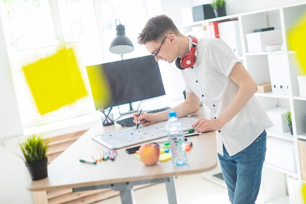 Ein junger Mann in Gläsern steht in der Nähe eines Computertisches