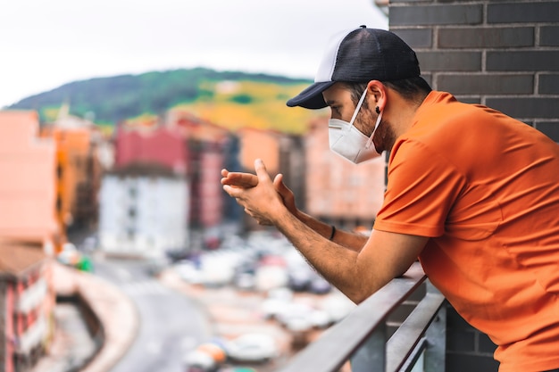 Ein junger Mann in Maske und orangefarbenem Hemd applaudierte um 8 Uhr nachmittags auf dem Balkon. Pandemisches Coronavirus in Spanien