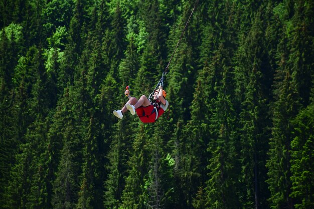 Ein junger Mann ist vom Bungee-Jumping gesprungen und hängt nun an einem Seil und filmt sich auf einer Sportvideokamera vor einem verschwommenen Hintergrund eines grünen Waldes