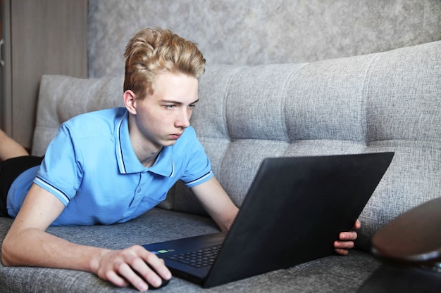 Ein junger Mann lag auf dem Sofa und benutzte zu Hause einen Laptop, Fernunterricht