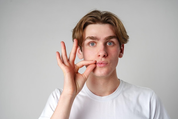 Ein junger Mann macht eine Handgestur in der Nähe des Gesichts vor einem klaren Hintergrund