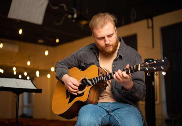 Ein junger Mann mit Bart spielt eine Akustikgitarre in einem Raum mit warmer Beleuchtung