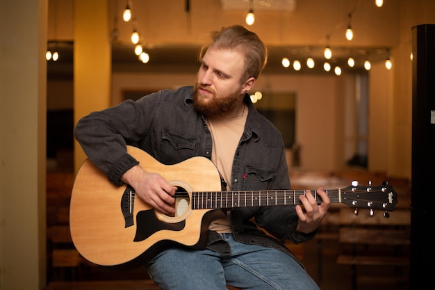 Ein junger Mann mit Bart spielt eine Akustikgitarre in einem Raum mit warmer Beleuchtung