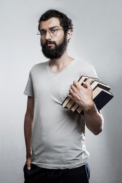 Ein junger Mann mit Brille und Bart hält einen Stapel Bücher in den Händen. Schul-und Berufsbildung.