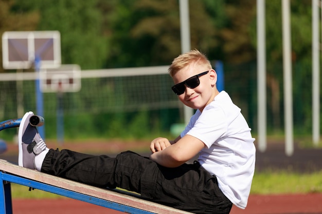 Ein junger Mann mit dunkler Brille trainiert im Sommer auf dem Sportplatz die Muskeln der Presse. Foto in hoher Qualität