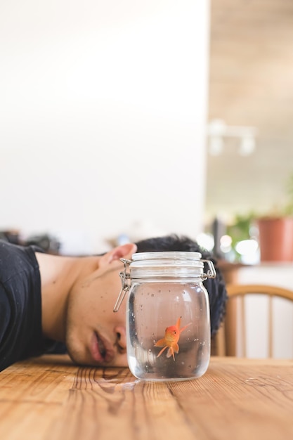 Foto ein junger mann mit einem goldfisch in einem glas auf dem tisch zu hause