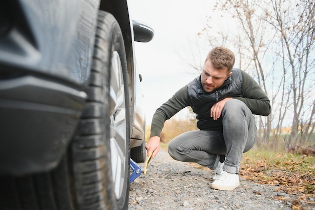 Ein junger Mann mit einem schwarzen Auto, das auf dem Straßenkopierplatz eine Panne hatte