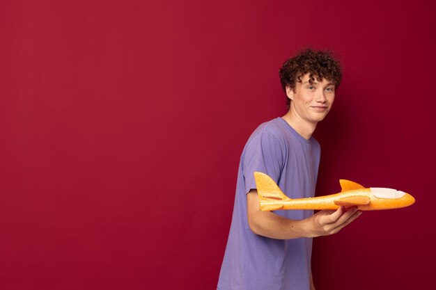 Ein junger Mann mit einem Spielzeugflugzeug in einem purpurroten T-Shirt mit unverändertem rotem Hintergrund