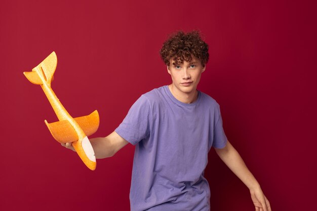 Ein junger Mann mit einem Spielzeugflugzeug in einem purpurroten T-Shirt mit unverändertem rotem Hintergrund