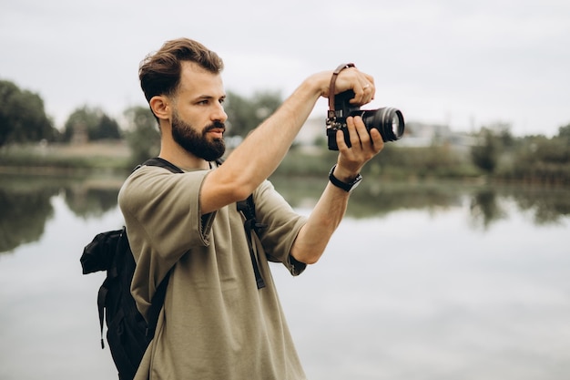 Ein junger Mann mit einer modernen SLR-Kamera in den Händen auf einem natürlichen Hintergrund