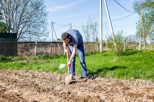 Ein junger Mann mit einer Schaufel auf einem Feld. Landwirtschaft und traditionelle Frühlingsfarmarbeit. Kartoffeln pflanzen im Mai.