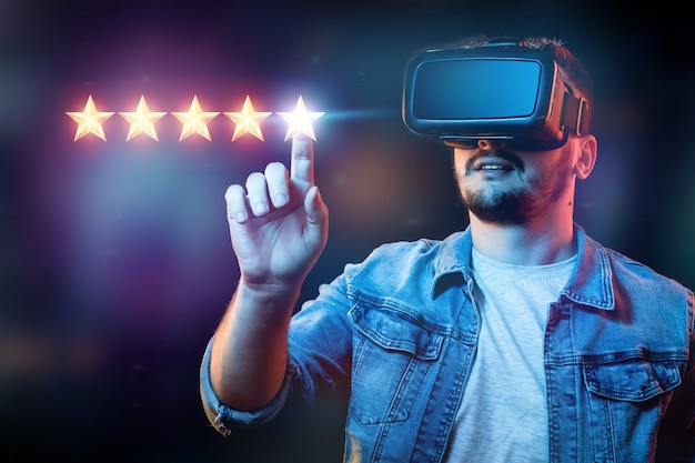 Ein junger Mann mit einer Virtual-Reality-Brille setzt 5 Sterne und vergibt eine neue Bewertung, Bewertungsdienste, ein neues Geschäftskonzept.