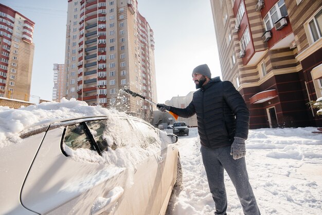 Ein junger Mann putzt sein Auto nach einem Schneefall an einem sonnigen, frostigen Tag.