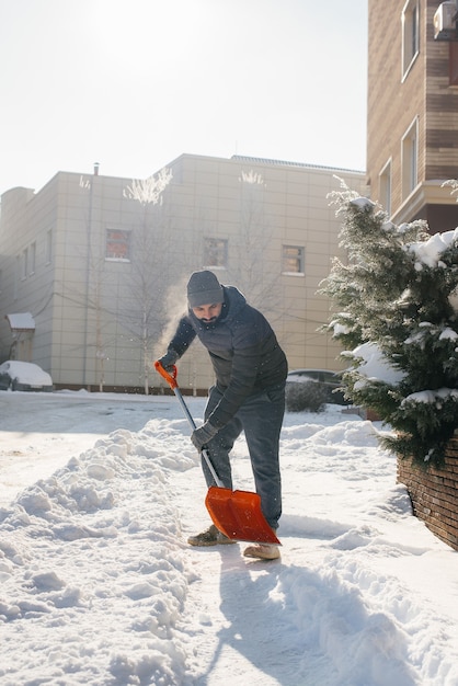 Ein junger Mann räumt an einem sonnigen und frostigen Tag den Schnee vor dem Haus. Die Straße vom Schnee säubern.