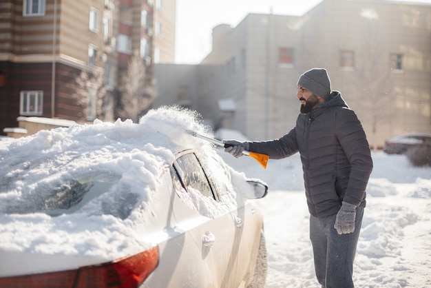 Ein junger Mann reinigt sein Auto nach einem Schneefall an einem sonnigen, frostigen Tag.