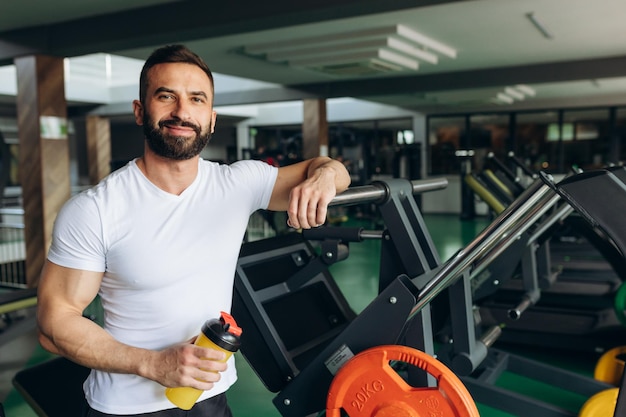 Ein junger mann ruht sich nach dem training im fitnessstudio aus und hält einen shaker in der hand fitness- und trainingskonzept