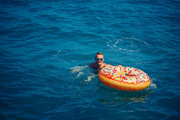 Ein junger Mann schwimmt auf einem aufblasbaren Luftringkreis im Meer mit blauem Wasser Festlicher Urlaub an einem fröhlichen sonnigen Tag