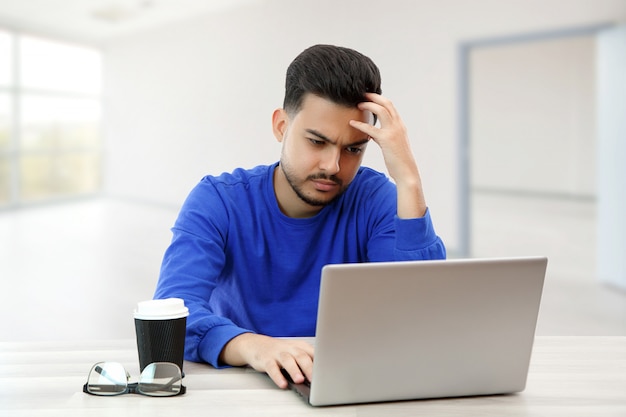 Ein junger Mann sitzt an einem Laptop auf der Suche nach Arbeit im Internet und macht Geschäfte im globalen Netzwerk mit einer Tasse Kaffee. auf Licht