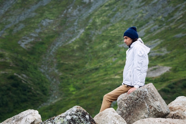 Ein junger Mann sitzt auf einem Stein hoch in den Bergen und bewundert die Natur. Schöne Naturlandschaft.