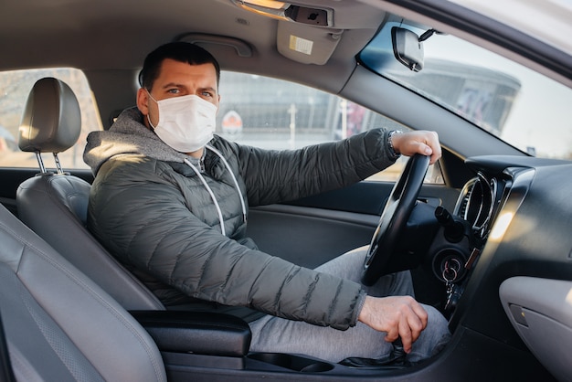 Ein junger Mann sitzt hinter dem Lenkrad und trägt eine Maske für die persönliche Sicherheit, während er während einer Pandemie und eines Coronavirus fährt. Epidemie.