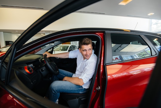 Ein junger Mann sitzt in der Kabine eines neuen Autos und testet es. Ein Auto kaufen.