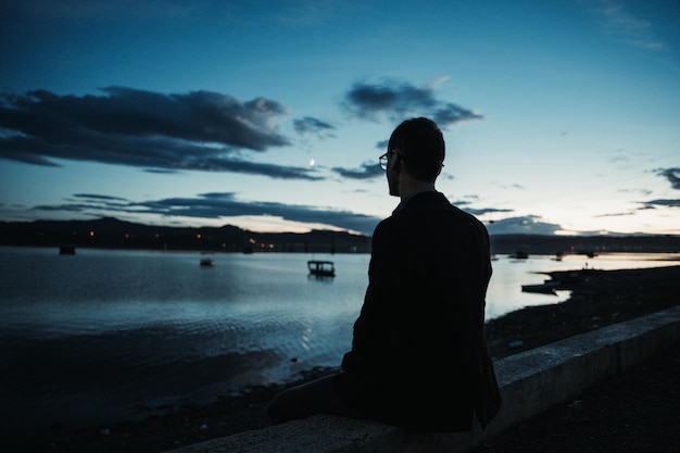 Ein junger Mann sitzt und beobachtet den Sonnenuntergang am See