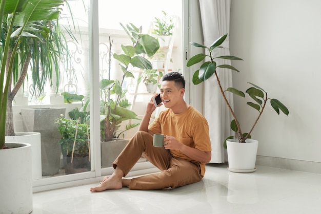 Ein junger Mann sitzt zu Hause auf dem Boden im Wohnzimmer,