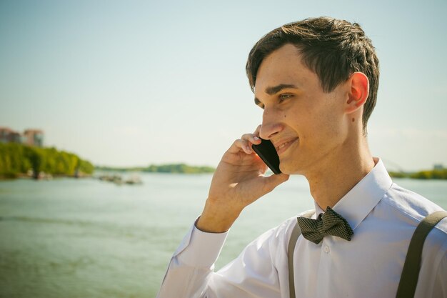 Ein junger Mann spricht am Handy und steht am Flussufer vor klarem Himmel