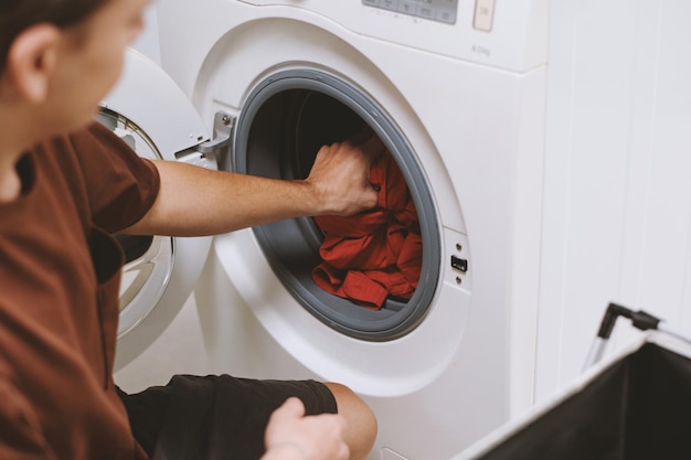 Ein junger Mann steckt schmutzige Kleidung in die Waschmaschine