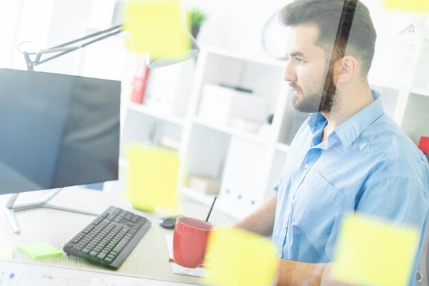 Ein junger Mann steht im Büro in der Nähe eines transparenten Brettes mit Aufklebern.