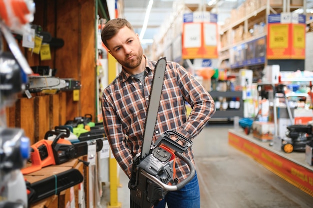 ein junger Mann steht mit einer neuen elektrischen Säge im Werkzeugladen