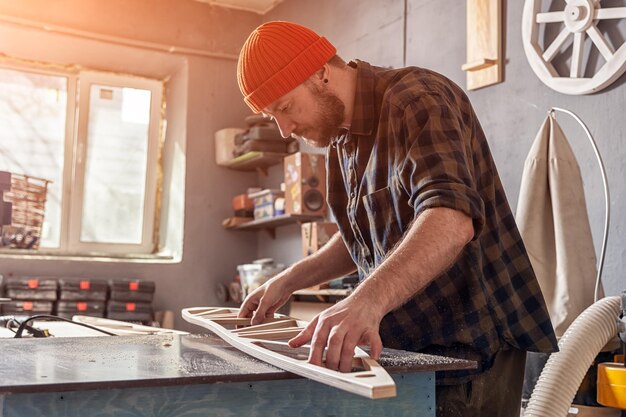 Foto ein junger mann tischlerbauer in arbeitskleidung, der ein holzbrett mit einer fräsmaschine in der werkstatt um viele geräte herum bearbeitet holzbretter reparaturkonzepte für zu hause