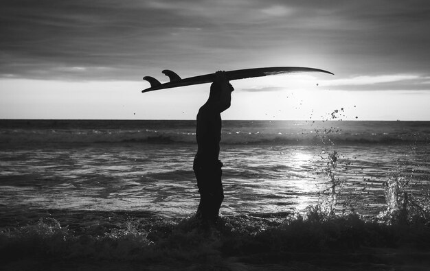 Foto ein junger mann trägt ein surfbrett auf dem kopf, während er am strand steht
