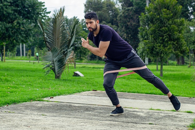Ein junger Mann trainiert mit Elastikschnüppeln und macht im Freien in einem Park Hockenbeinübungen