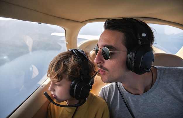 Ein junger Mann und sein Sohn mit Kopfhörern fliegen in einem Flugzeug über dem Meer und schauen mit Interesse aus dem Fenster