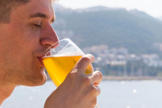 Ein junger Mann versucht am frühen Morgen am Strand Bier zu trinken