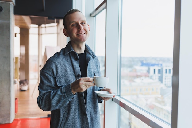 Ein junger Mann von europäischem Aussehen im Freizeitanzug trinkt Kaffee und schaut aus dem Fenster