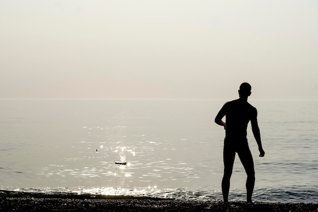 Ein junger Mann wirft Steine ins Wasser Silhouetten