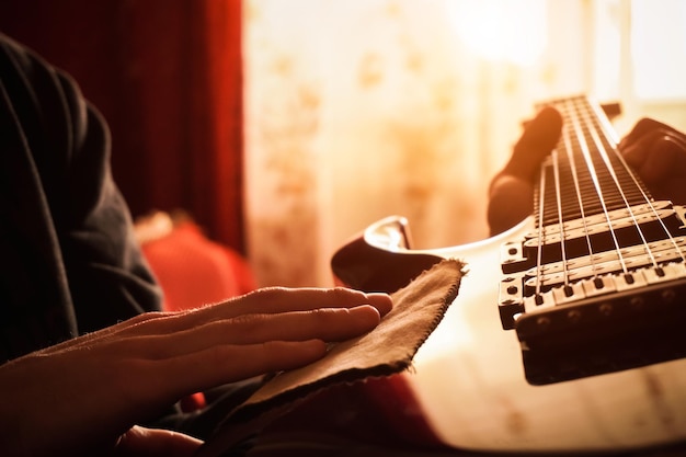 Ein junger Mann wischt Staub von Sonnenstrahlen einer E-Gitarre ab