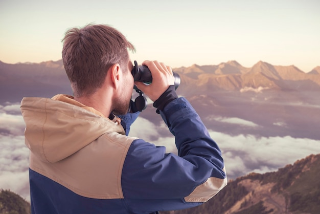 Ein junger Mensch, der in den Bergen wandert und ein Fernglas verwendet, Reisekonzept