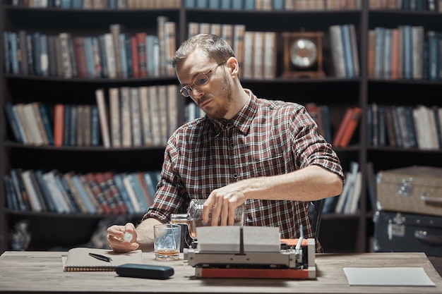 Ein junger Schriftsteller sucht Inspiration, sitzt am Schreibtisch und trinkt Alkohol