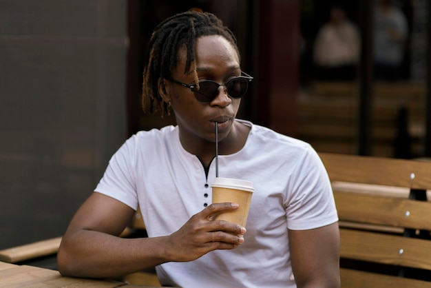 Ein junger schwarzer Mann sitzt draußen im Café und trinkt eine Tasse Kaffee während der Kaffeepause