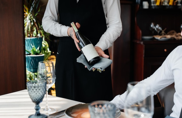 Ein junger Sommelier in stilvoller Uniform demonstriert und bietet dem Kunden im Restaurant erlesene Weine an Kundenservice Gedeckter Tisch in einem feinen Restaurant