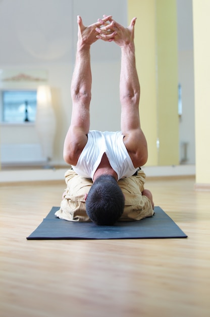 Ein junger starker Mann, der sitzende Yogaübungen macht. Adho Mukha Virasana im Yoga-Studio