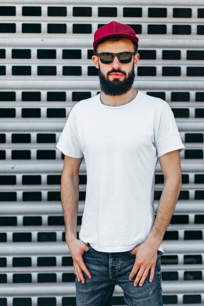 Ein junger stilvoller Mann mit einem Bart in einem weißen T-Shirt und einer Brille