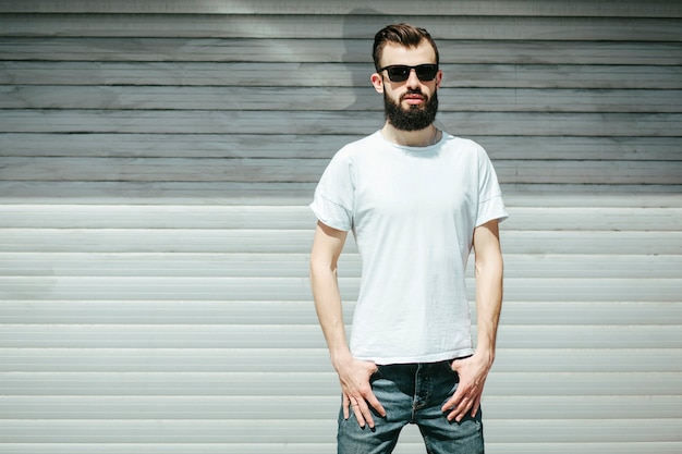 Ein junger stilvoller Mann mit einem Bart in einem weißen T-Shirt und einer Brille